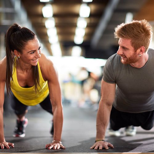 Mann und Frauen schauen sich während einer Liegestütze im Active Fitnessstudio Bad Laasphe an und lächeln 